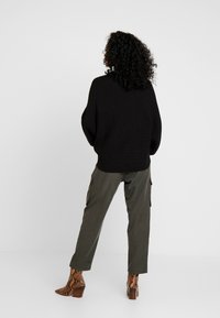 Pull noir en tricot à coupe décontractée, associé à un pantalon cargo vert olive et des bottines à imprimé serpent marron à talon carré.