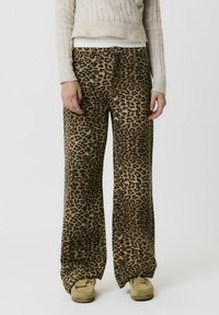 Pantalones de pierna ancha con estampado de leopardo en tela color marrón y negro, con cierre de botón y bolsillos frontales. Textura suave y ajuste relajado.