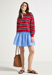 Polo a maniche lunghe a righe rosse e bianche, abbinato a una gonna azzurro chiaro. Una borsa marrone e sandali flat completano il look.