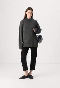 Mörkgrå oversized tröja med hög halsringning, svarta cropped byxor och svarta slip-on skor. Modellen håller en liten svart väska.
