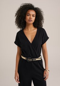 Svart strukturerad jumpsuit med en djup V-hals, korta uppvikta ärmar och ett kontrasterande beige bälte. Slät tyg med en avslappnad passform.