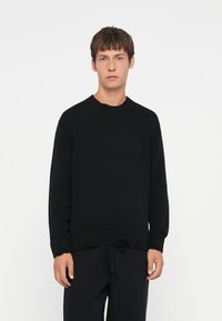 Schwarzer Strickpullover mit geripptem Rundhalsausschnitt und Säumen. Verfügt über eine strukturierte Oberfläche und eine lockere Passform. Kombiniert mit dunklen Hosen.