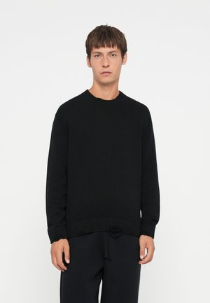 Black knit sweater with ribbed crew neck and hem. Features a textured finish and relaxed fit. Paired with dark trousers.