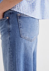 I jeans in denim blu chiaro presentano un design classico a cinque tasche e dettagli di cucitura sottili sulle cuciture e sulle tasche.
