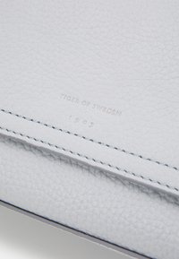 Portafoglio in pelle grigio chiaro con superficie texture, cuciture a contrasto e branding in rilievo "TIGER OF SWEDEN 1903."