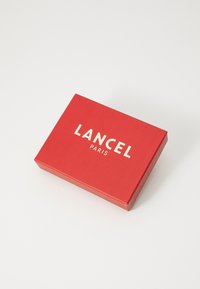 Red cardboard box with white text "LANCEL PARIS" on top. Smooth texture, rectangular shape, with sharp edges and no additional patterns.
