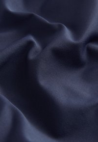 Tissu bleu foncé lisse avec des plis doux et une fine texture côtelée visible sous un éclairage doux.
