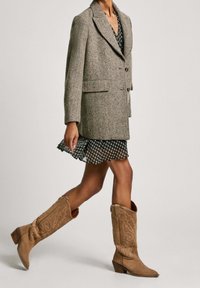 Dwurzędowa marynarka w wzór houndstooth z wełny, połączona z czarno-białą sukienką w kwiaty oraz brązowymi zamszowymi kowbojkami z haftem.