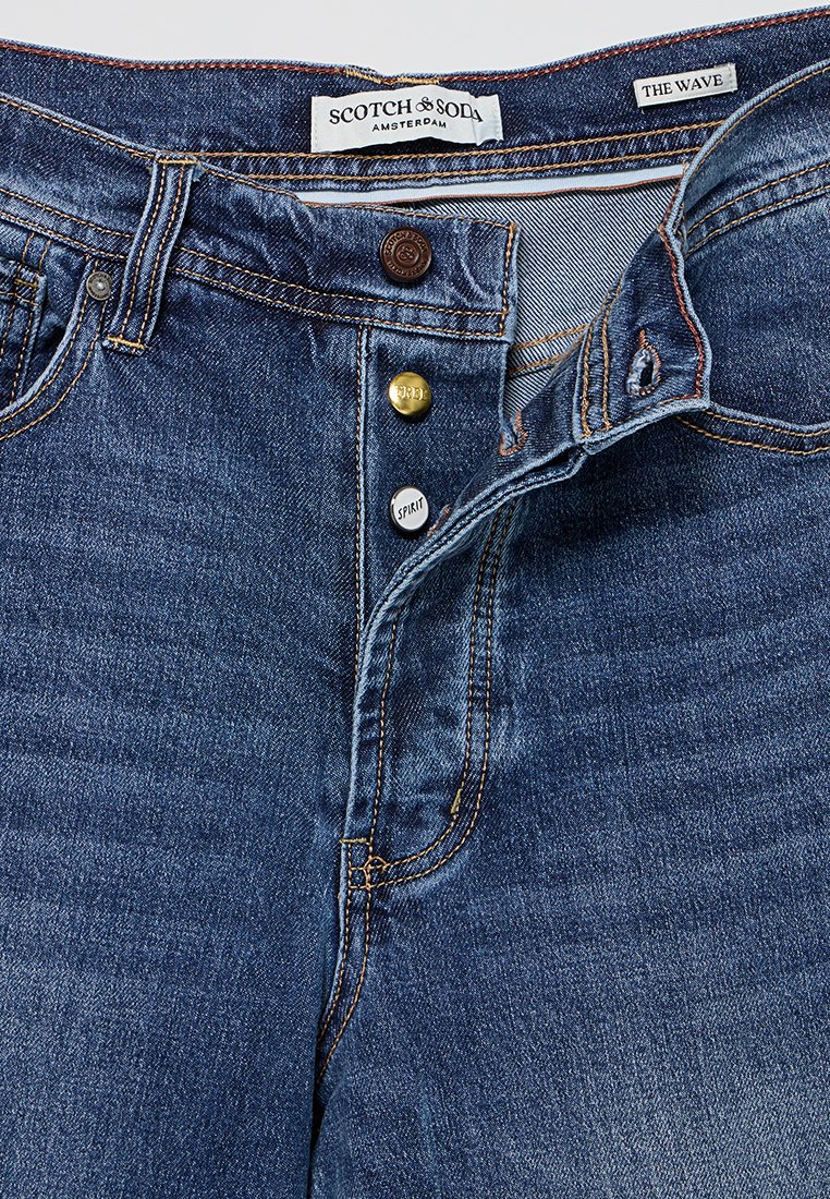 Blaue Denim-Jeans mit Knopfleiste, drei sichtbaren Knöpfen mit der Gravur "RRL", "SPIRIT" und einem braunen Markenknopf, Etiketten "Scotch & Soda" und "The Wave."