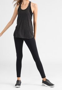 Black athletic tank top with racerback design, layered over fitted black leggings and matching sneakers. Lightweight fabric with smooth texture.