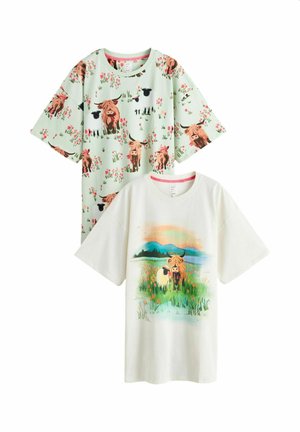 Dvě košile s krátkým rukávem: jedna mátově zelená s opakujícím se vzorem krav a ovcí, druhá bílá s motivem krav a ovcí v květinovém poli s horským pozadím.