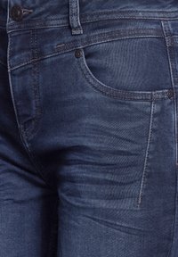 Denim jeans in dark blue, featuring a classic five-pocket design, subtle whiskering, and contrasting stitching. Button fastener at the waist.