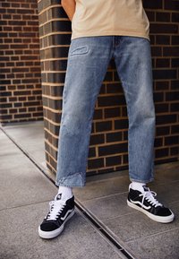 Ljust blå denimjeans med ett slitna lappar, rak passform och fransad fåll. I kombination med svarta och vita sneakers samt ankelsockor.