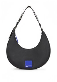 Svart läderväska med böjd form, med en blå fyrkantig logotypmärke och ett avtagbart band med ett kontrasterande mönster.