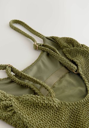 Grøn badedragt med tekstureret stof, der har ruching, justerbare stropper og en glat indvendig foring. Accenteret med guldtone hardware.