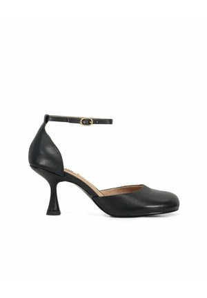 Décolleté in pelle nera con tacco medio, punta arrotondata e sottile cinturino alla caviglia con piccola fibbia dorata, su sfondo bianco.