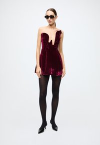 Burgundy velvet mini dress with a deep V-neck, asymmetrical shoulder, paired with black opaque tights and black pointed heels.