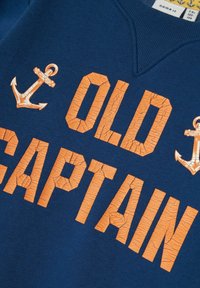 Sudadera marina con texto agrietado en naranja "OLD CAPTAIN" y dos gráficos de ancla en naranja. Presenta un escote en V y una textura de tela suave.