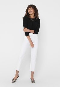 Black long-sleeve top, white straight-leg jeans, and patterned pointed-toe flats. Minimalist design with a smooth texture.