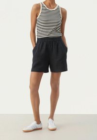Shorts en lin noir avec une taille élastique et des poches latérales, associés à un débardeur rayé et des baskets blanches. Design simple et décontracté.