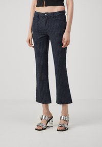 Marineblauwe geprinte crop pants met een subtiele logodruk, met een klassieke pasvorm, voorzakken en een onafgewerkte zoom. Gecombineerd met zilveren sandalen.