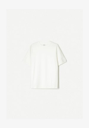 Bela kratka majica s kratkimi rokavi iz mehkega bombaža. Oblečen kroj s sproščenim prileganjem in brez vidnih logotipov ali vzorcev.