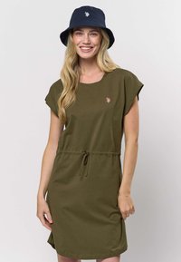 Bavlnené šaty olivovo zelenej farby s krátkymi rukávmi, sťahované v páse šnúrkou a ružovým vyšívaným logom. Kombinované s tmavomodrým klobúkom typu bucket.