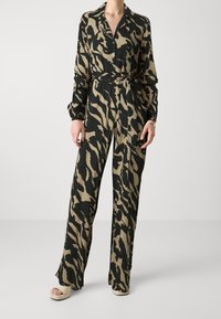 Jumpsuit à imprimé animal noir et beige avec des manches longues, un col, une taille ceinturée et des pantalons évasés ; fabriqué à partir d'un tissu léger.