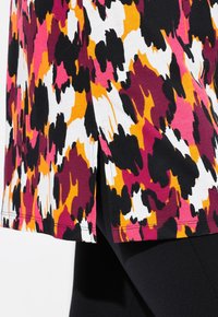 Buntes Oberteil mit einem auffälligen abstrakten Muster in Pink, Gelb, Schwarz und Weiß. Verfügt über seitliche Schlitze und eine sanfte Stofftextur.