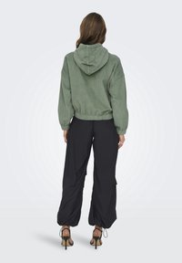 Zielona kordurowa cropped bluza z kapturem, w połączeniu z luźnymi czarnymi spodniami i brązowymi szpilkami. Teksturowany materiał z elastycznymi mankietami.