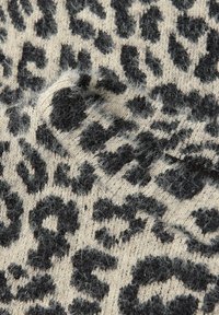 Neulekangas, jossa on musta leopardikuosi vaalean kermaisen taustan päällä. Kangas on pehmeä ja pörröinen, ja näkyvissä on neulontasaumoja.