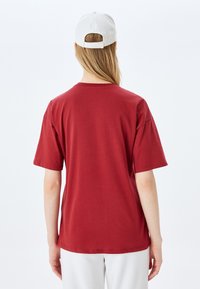 Camiseta de algodón color marrón con mangas cortas, corte relajado, escote redondeado y diseño liso en la parte posterior. Combinada con una gorra de béisbol blanca.