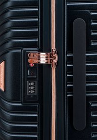 Valigia nera rigida con texture a righe, zip in oro rosa, doppie serrature e un pannello con lucchetto a combinazione sul lato.