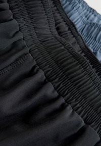 Schwarzer und dunkelblauer Stoff mit geraffter Textur, der die details des dehnbaren Taillenbands und eine glatte Oberfläche zur Schau stellt. Keine sichtbaren Muster oder Metallteile.