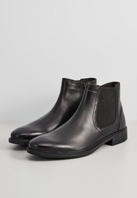 Botas de tobillo de cuero negro con paneles laterales elásticos, punta redonda y tacón bajo apilado. Textura suave y diseño minimalista.