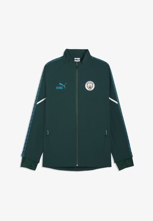 Donkergroene sportjas met ritssluiting, voorzien van het Manchester City-logo en het Puma-logo, met geparpatternde strepen op de mouwen en ritszakken aan de zijkant.