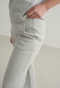 Grå sweatpants lavet af blødt stof, med en elastisk talje, sidelommer og et lille mærketikette på låret.