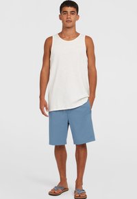 Un débardeur de couleur claire et un short bleu. Le débardeur est simple avec une coupe décontractée. Le short est de longueur genou avec un cordon de serrage et des poches latérales.