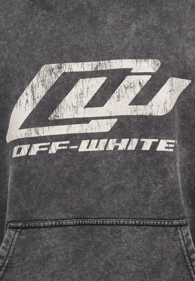Feszült fehér "OFF-WHITE" felirat és szögletes logó nyomtatva sötétszürke texturált anyagra, egy varrás és zsebnél nyitás fölött.