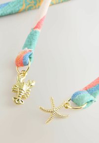 Colorful fabric bracelet with gold lobster and starfish charms on a light background.