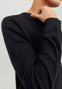 Schwarzer Strickpullover mit Rundhalsausschnitt, gerippten Bündchen und einfachem Design; Nahaufnahme von Ärmel- und Schulteredetail.