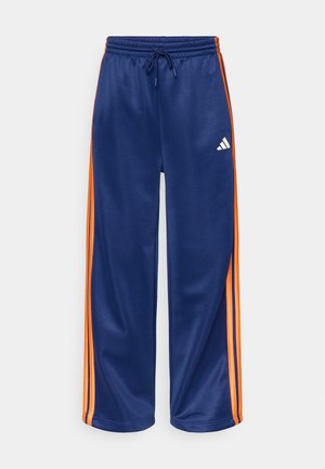 Calças de treino azuis-marinho com riscas laterais laranja, feitas de tecido macio, com cintura elástica e um pequeno logótipo branco na frente.