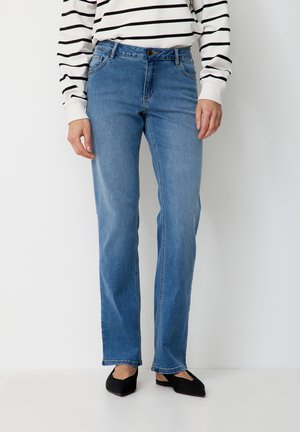 Person wearing light blue straight-leg jeans, black pointed flats, and a white long-sleeve shirt with black horizontal stripes.