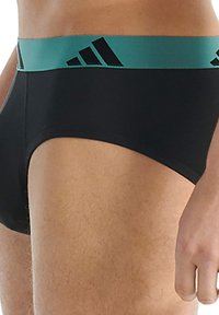 Černé boxerky s tyrkysovým elastickým pásem, na kterém jsou tři černé pruhy. Materiál je hladký a dobře obepíná tělo.