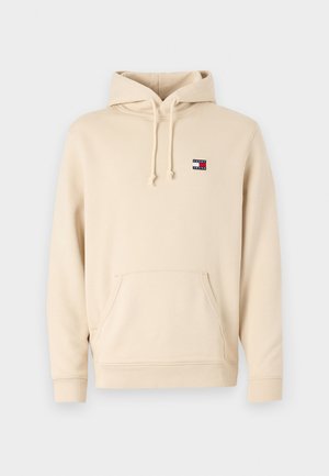Beige hettegensere laget av myk stoff, med frontlomme og ribbede mansjetter. Lite logo-merke på øvre venstre bryst.