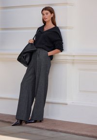 Anthrazitgrauer Wollpullover mit weitem Kragen, kombiniert mit hoch taillierter, locker sitzender grauer Karohose. Schwarze, strukturierte Handtasche und spitze Absätze.