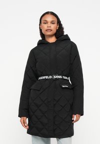 Cappotto nero trapuntato con cappuccio, dotato di vita con cinturino e accenti del logo. Due tasche frontali e texture a motivo diamante. Vestibilità casual.