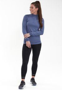 Langærmet, kvart-zip atletisk top i lys blå, parret med sorte leggings. Har en glat tekstur og tætsiddende design.