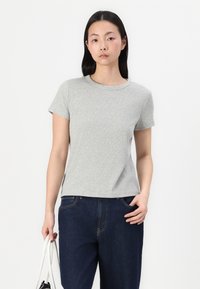 Grå kortærmet T-shirt med rund halsudskæring og en glat bomuldsstruktur, båret med mørkeblå jeans. Modellen holder en hvid taske.