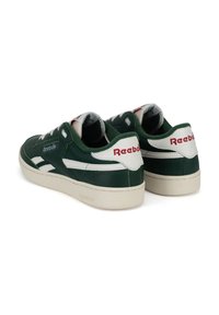 Pár tmavozelených a bielych tenisiek Reebok s červeným vyšívaným logom a béžovými podrážkami, zobrazených z zadného a bočného uhla.